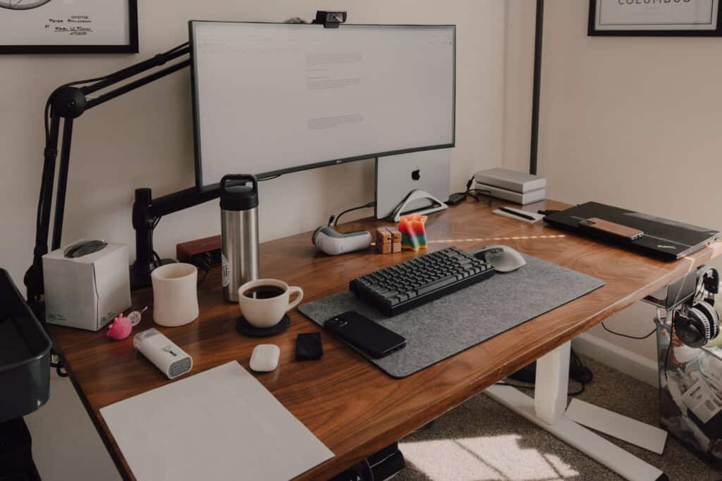 Walnut desk covered in desktop clutter such as an extended mousepad, a keyboard, mouse, fidget toys, papers, and coffee mugs, it feels antithetical to minimalism.